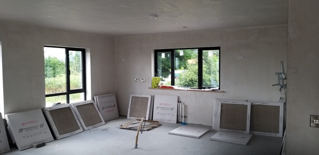 A Partially Constructed Room with Bare Plastered Walls, Large Windows Showing Greenery Outside — Alpha and Omega Refurbishment in Tuam, Galway